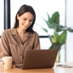 Portrait of smiling woman working on laptop with coffee